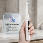 A close-up shot of a hand holding a white electric toothbrush, featuring a clean "30s reminder" graphic explaining the smart pause technology for changing cleaning areas.