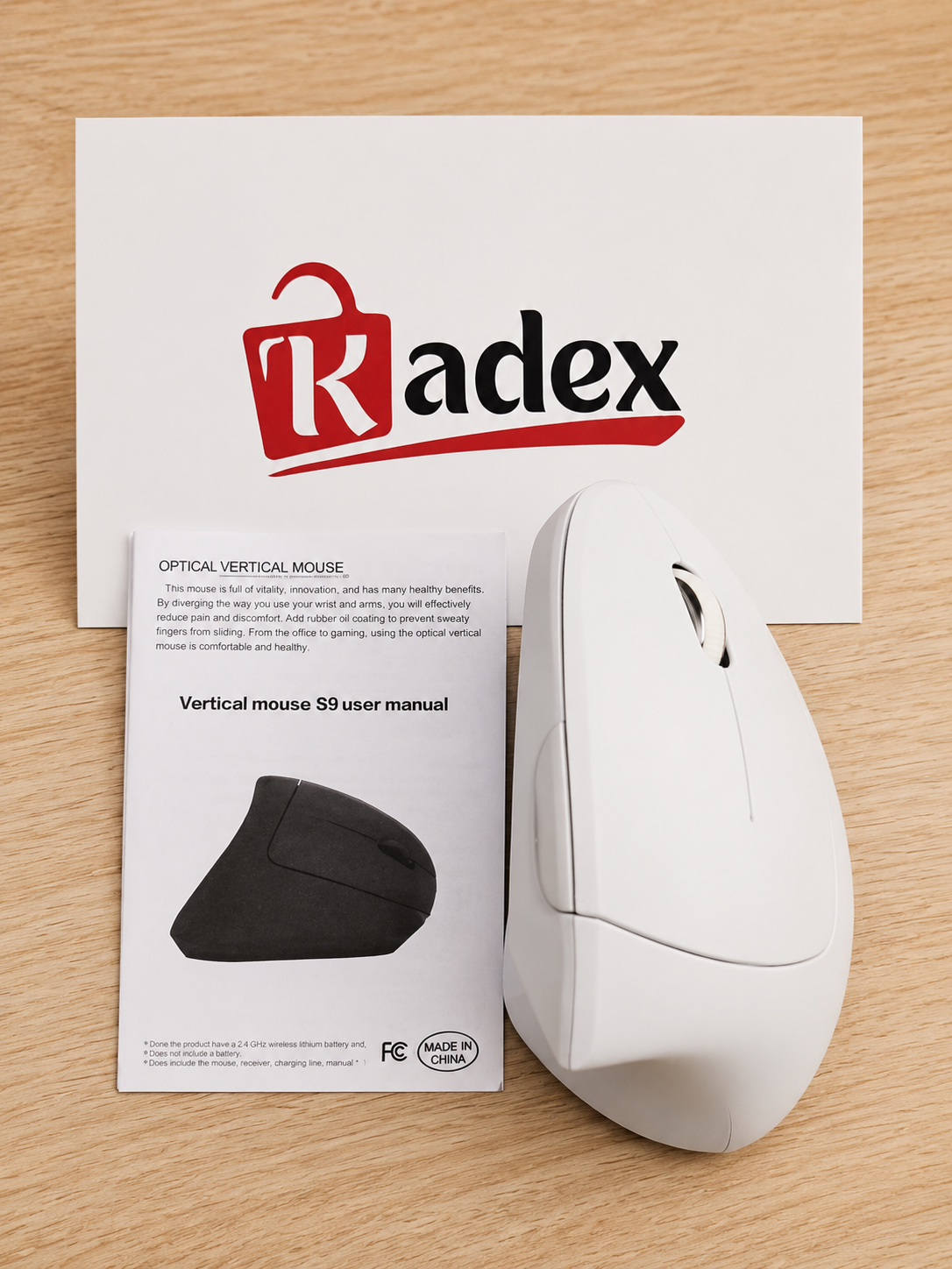 A white optical vertical mouse shown next to its user manual and a branded Radex card on a light wood surface.