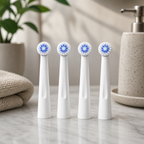 Four white electric toothbrush replacement brush heads with blue bristles arranged on a marble bathroom counter, with a soft towel, plant, and soap dispenser in a clean, natural setting.